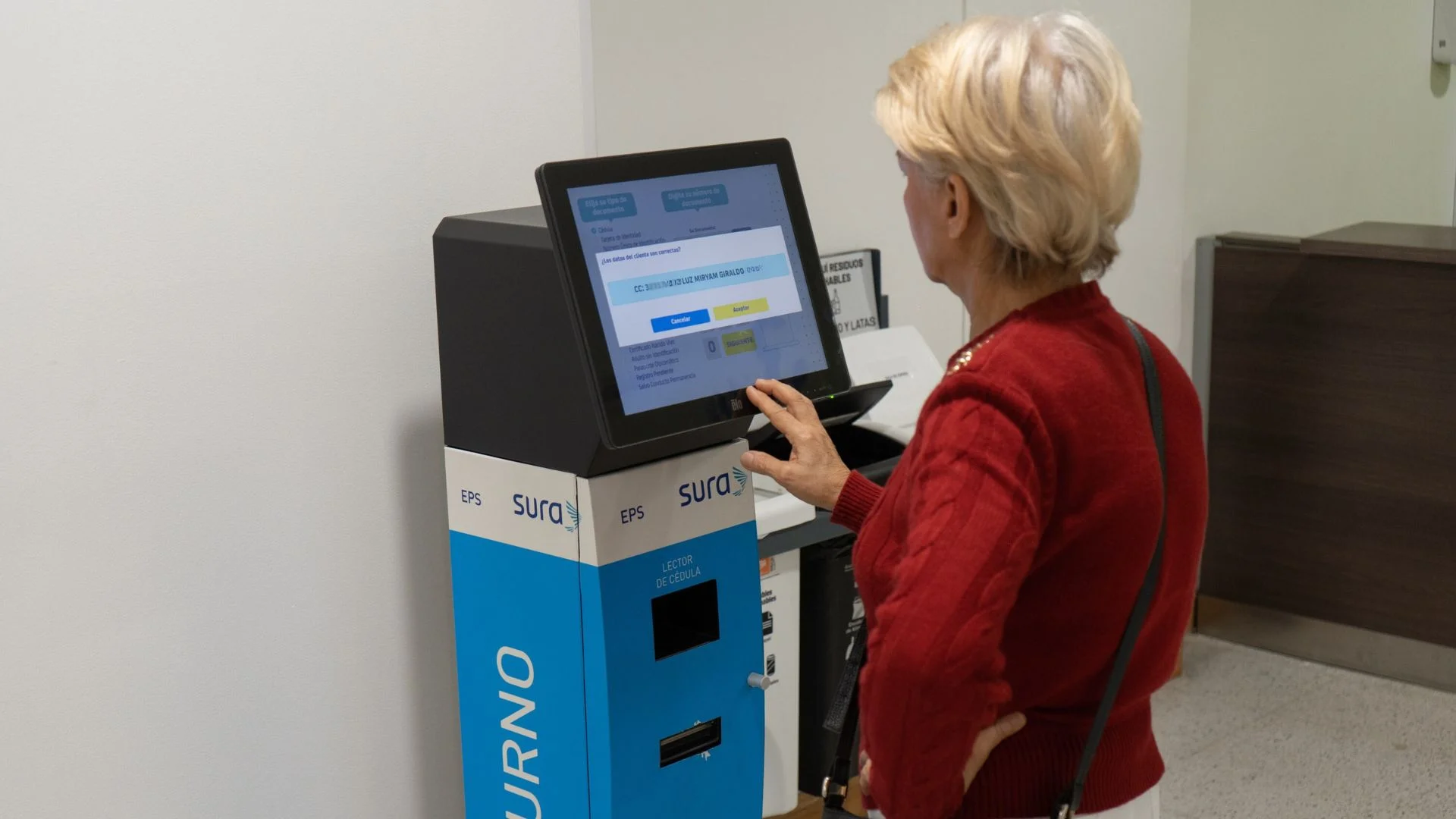 Mujer mayor interactuando fluidamente con un kiosco táctil de autogestión de turnos de Qanty en una sucursal